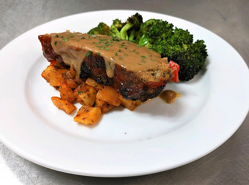 A photo of meatloaf on a plate with broccoli and seasoned potatoes on the side