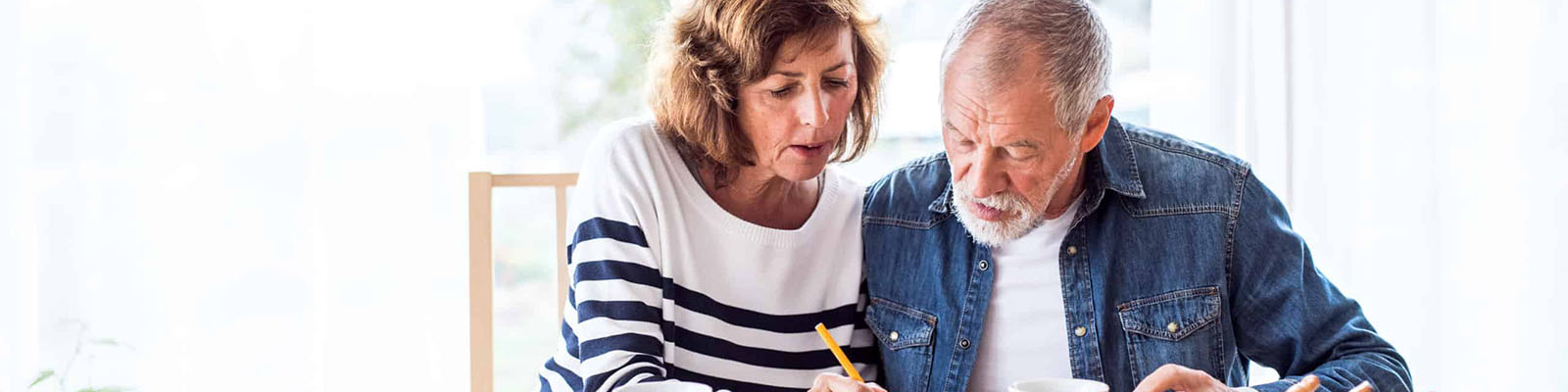 A senior man and senior woman sitting at a table filling out a document with a pencil